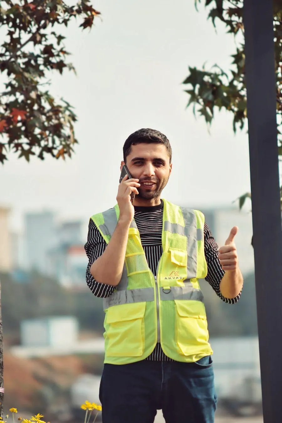 Handwerker in Warnweste am Telefon, Daumen hoch